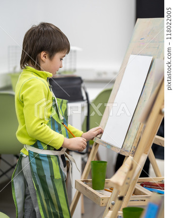 Little boy draws in studio. Art therapy, art education for children. Painting on paper on easel. Developing fine motor skills. Mock up. Little boy draws in studio. Art therapy, art education for children. Painting on paper on easel. Developing fine motor skills. Mock up. 118022005