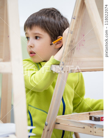 Little boy draws in studio. Art therapy, art education for children. Painting on paper on easel. Developing fine motor skills and imagination. Little boy draws in studio. Art therapy, art education for children. Painting on paper on easel. Developing fine motor skills and imagination. 118022074