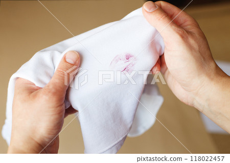 man holding a white shirt with a dirty stain from red kiss lipstick. 118022457