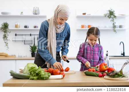 Muslim mother and daughter preparing salad together in kitchen 118022816