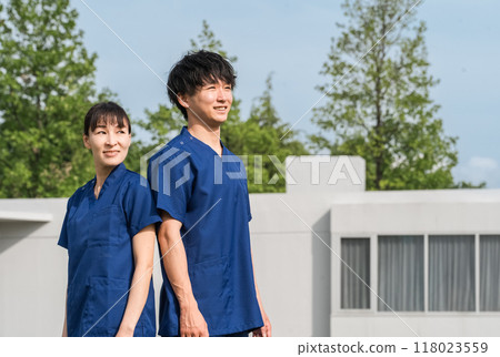 醫院和設施前穿著手術服的男女醫護人員（護士、護理人員、護理人員） 118023559