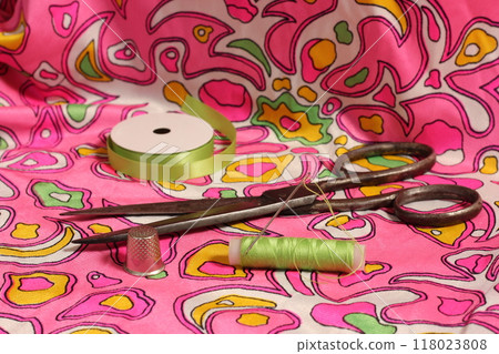 Spool of Green Thread, Thimble and Needle on Retro Pink and Green Fabric 118023808