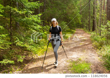 Beautiful woman with Scandinavian sticks hiking in summer through a forest by path. 118024056