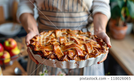 Close up of a woman wearing apron holds an apple pie in a kitchen. Background for of the Thanksgiving seasonal or bakery and pastry business. AI generated. 118026065