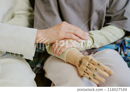 Close-up of two individuals holding hands, offering comfort and support. One person has prosthetic limb, showcasing moment of connection and care 118027589