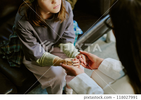 Child sitting on couch, receiving comfort from person holding robotic hand, reflecting support and technological advancement. Details emphasize childs thoughtful expression 118027991
