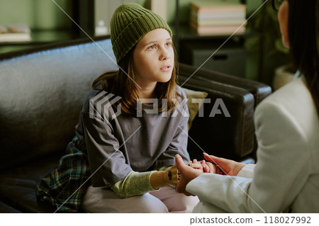Child wearing casual clothing sits on couch holding hands with therapist during therapy session in comfortable room Child wearing casual clothing sits on couch holding hands with therapist during therapy session in comfortable room 118027992