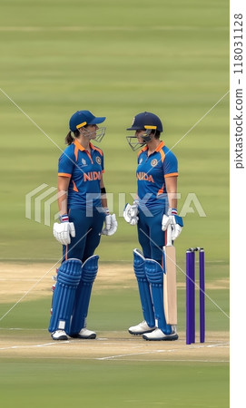 Two female cricket players in blue jerseys talking on the pitch, displaying teamwork and strategy before taking on the opposition. 118031128