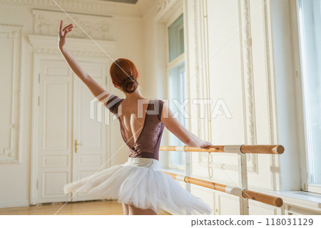 Young ballerina in tutu skirt stretching practicing ballet positions dancing near ballet barre in dance class. Young classical dancer woman in dance studio. Ballet class training Ballet school concept Young ballerina in tutu skirt stretching practicing ballet positions dancing near ballet barre in dance class. Young classical dancer woman in dance studio. Ballet class training Ballet school concept 118031129