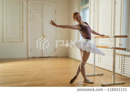 Young ballerina in tutu skirt stretching practicing ballet positions dancing near ballet barre in dance class. Young classical dancer woman in dance studio. Ballet class training Ballet school concept Young ballerina in tutu skirt stretching practicing ballet positions dancing near ballet barre in dance class. Young classical dancer woman in dance studio. Ballet class training Ballet school concept 118031131