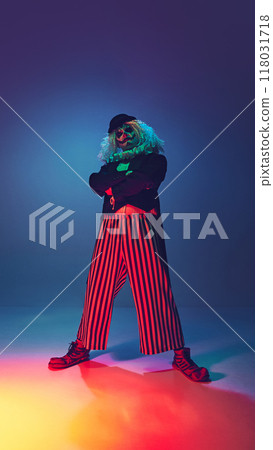 Tall and confident, clown crosses his arms and looking at camera in neon light against gradient background. Tall and confident, clown crosses his arms and looking at camera in neon light against gradient background. 118031718