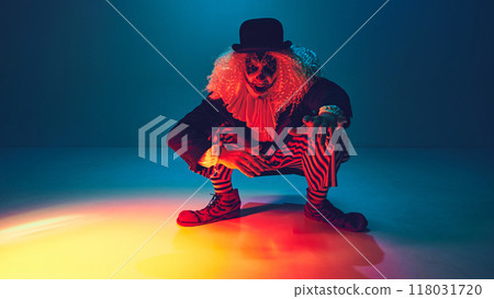 Crouched with menace, clown dressed retro clothes reaches forward, in neon light against gradient background. Crouched with menace, clown dressed retro clothes reaches forward, in neon light against gradient background. 118031720