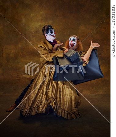 Two eerie clowns in playful interaction with exited expressions holds shopping bags in hand, posing against vintage backdrop. 118031835