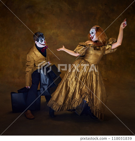 Two clowns with frightening make-up, one bending under weight of black shopping bags, while other poses against vintage backdrop. 118031839