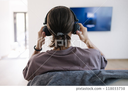 Back view of teenage boy puts on headphones and conceded to tv for listening podcast Back view of teenage boy puts on headphones and conceded to tv for listening podcast 118033738