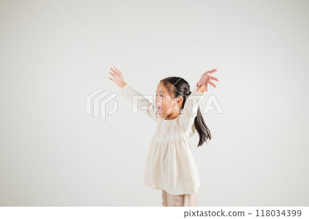 A jubilant kid girl raises her fists in celebration of her success, saying yes with excitement. Asian portrait of a happy young kindergarten child in a studio shot on a white background, winning 118034399