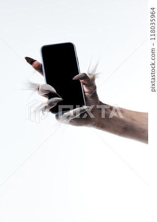 Werewolf's hand with long fingers and nails, paw holding modern smartphone with blank screen against white studio background. Werewolf's hand with long fingers and nails, paw holding modern smartphone with blank screen against white studio background. 118035964