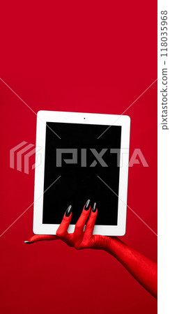 Horror red devil's hand with blank long nails holding tablet with blank screen against red studio background. Horror red devil's hand with blank long nails holding tablet with blank screen against red studio background. 118035968