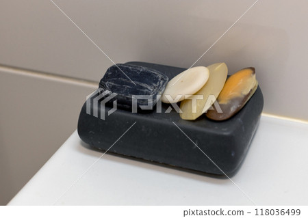 Variety of used soap bars resting in a black soap dish in a bathroom. Variety of used soap bars resting in a black soap dish in a bathroom. 118036499