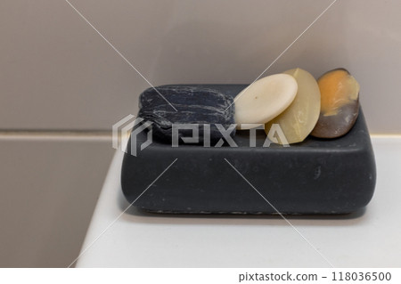 Three soap bars of different colors placed on a black soap dish, captured in a minimalist bathroom setting. Three soap bars of different colors placed on a black soap dish, captured in a minimalist bathroom setting. 118036500