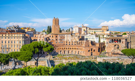 The ancient Trajan Market stands proudly in Rome, Italy, showcasing its remarkable architecture while surrounded by blooming greenery and majestic ancient ruins under a bright blue sky. 118036527