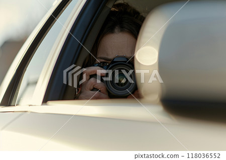 A person conducting surveillance during daylight hours, capturing photos from a car window with a professional camera. A person conducting surveillance during daylight hours, capturing photos from a car window with a professional camera. 118036552