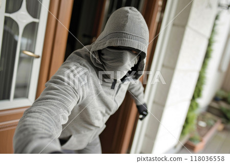A hooded intruder leaning into a doorway, ready to break in, wearing a gray outfit. A hooded intruder leaning into a doorway, ready to break in, wearing a gray outfit. 118036558