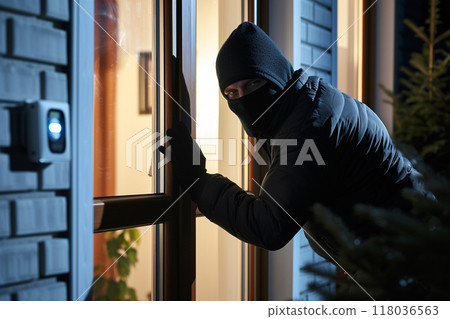 A masked burglar peering through a window at night, attempting to break in. A masked burglar peering through a window at night, attempting to break in. 118036563