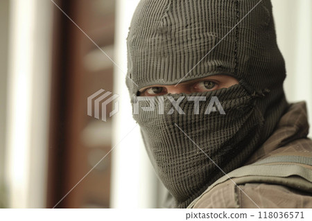 A man wearing a mask stands outdoors in a gritty urban environment, with a serious expression. 118036571