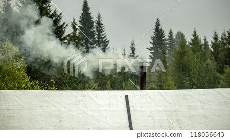 the iron pipe of the village bath, from which smoke comes out against the background of the forest the iron pipe of the village bath, from which smoke comes out against the background of the forest 118036643