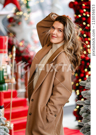 A beautiful woman in a white sweater and coat stands against the background of Christmas decorations, bokeh, holiday mood 118036653