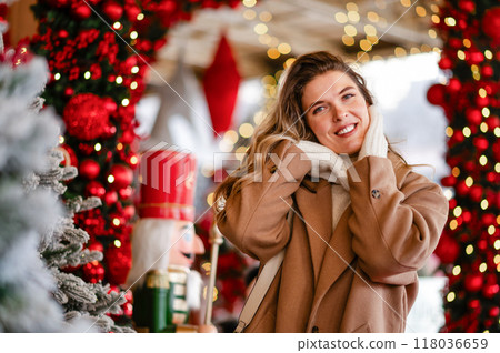 A beautiful woman in a white sweater and coat stands against the background of Christmas decorations, bokeh, holiday mood 118036659