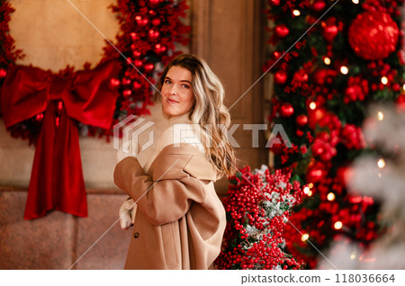 Beautiful woman in a coat and white mittens posing against the background of Christmas decorations, holiday mood Beautiful woman in a coat and white mittens posing against the background of Christmas decorations, holiday mood 118036664