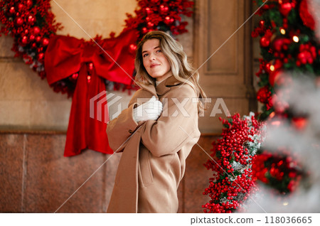 A beautiful woman in a white sweater and coat stands against the background of Christmas decorations, bokeh, holiday mood A beautiful woman in a white sweater and coat stands against the background of Christmas decorations, bokeh, holiday mood 118036665
