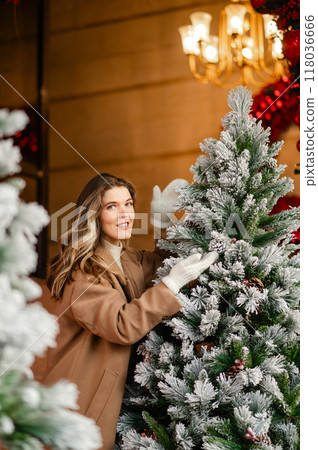 Beautiful woman in a coat and white mittens near the Christmas tree, holiday mood 118036666