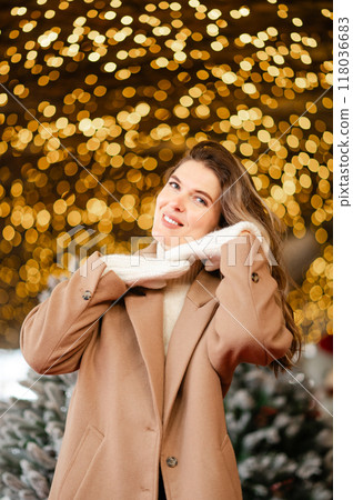 happy woman in a coat and white mittens stands in front of Christmas garlands, holiday mood 118036683