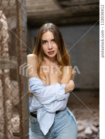 Woman in dropped off shoulders shirt posing near steel mesh fencing inside destroyed building 118036912