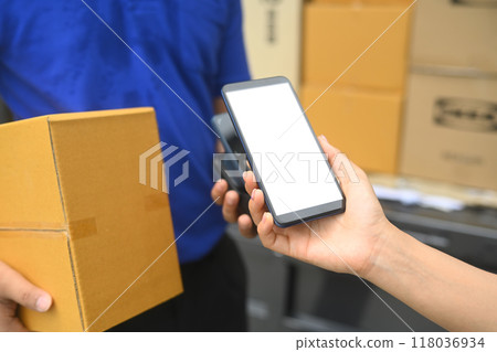 Woman making contactless payment with phone and received package from courier. Shipping and delivery services concept 118036934