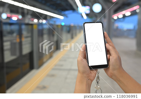 Close up of hands holding mobile phone with white screen against a blurred subway station background 118036991