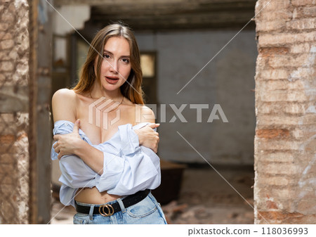 Woman in dropped off shoulders shirt posing near steel mesh fencing inside destroyed building 118036993