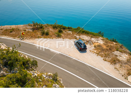 Car with a roof box, parked on the edge of a cliffside road, with the azure sea below reflecting the clear blue sky. Car with a roof box, parked on the edge of a cliffside road, with the azure sea below reflecting the clear blue sky. 118038228