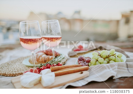 Charming rooftop picnic setup featuring rose wine glasses, cheese, grapes, croissant, and assorted snacks creating a relaxing ambiance for outdoor dining enjoyment Charming rooftop picnic setup featuring rose wine glasses, cheese, grapes, croissant, and assorted snacks creating a relaxing ambiance for outdoor dining enjoyment 118038375