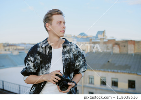 Caucasian man holding camera against urban rooftop background under clear sky, capturing details of buildings in daytime setting 118038516