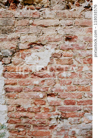 Detail of an aged brick wall with cracked, peeling plaster revealing underlying red and white bricks. The texture of the wall shows signs of erosion and structural wear Detail of an aged brick wall with cracked, peeling plaster revealing underlying red and white bricks. The texture of the wall shows signs of erosion and structural wear 118038576