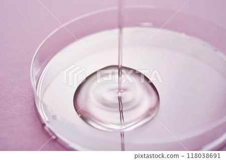 Serum or cosmetic oil flows into a transparent bowl on a purple background. 118038691