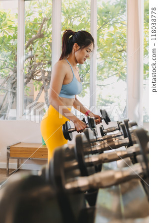 Woman in Yellow Blue fitness outfits picking up the dumbbells in the gym. 118038778