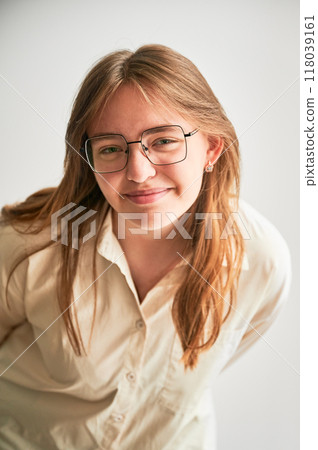 Portrait of beautiful girl smiling to camera. Cute girl in cream shirt and square glasses posing on white background. 118039161