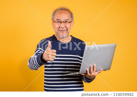 Portrait Asian old man wearing glasses use laptop computer and giving a thumbs up studio shot isolated yellow background, smiling happy elderly man gray haired concept of accomplishment satisfaction 118039982