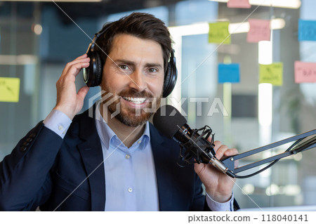 Confident man wearing headphones using microphone for podcast recording in office setting portrays professionalism and enthusiasm. Confident man wearing headphones using microphone for podcast recording in office setting portrays professionalism and enthusiasm. 118040141