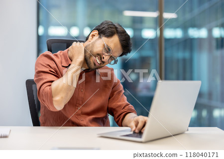 Office employee feeling neck pain while working on laptop. Professional in modern office showing signs of stress and discomfort, highlighting ergonomic issues common in workplace environments. Office employee feeling neck pain while working on laptop. Professional in modern office showing signs of stress and discomfort, highlighting ergonomic issues common in workplace environments. 118040171